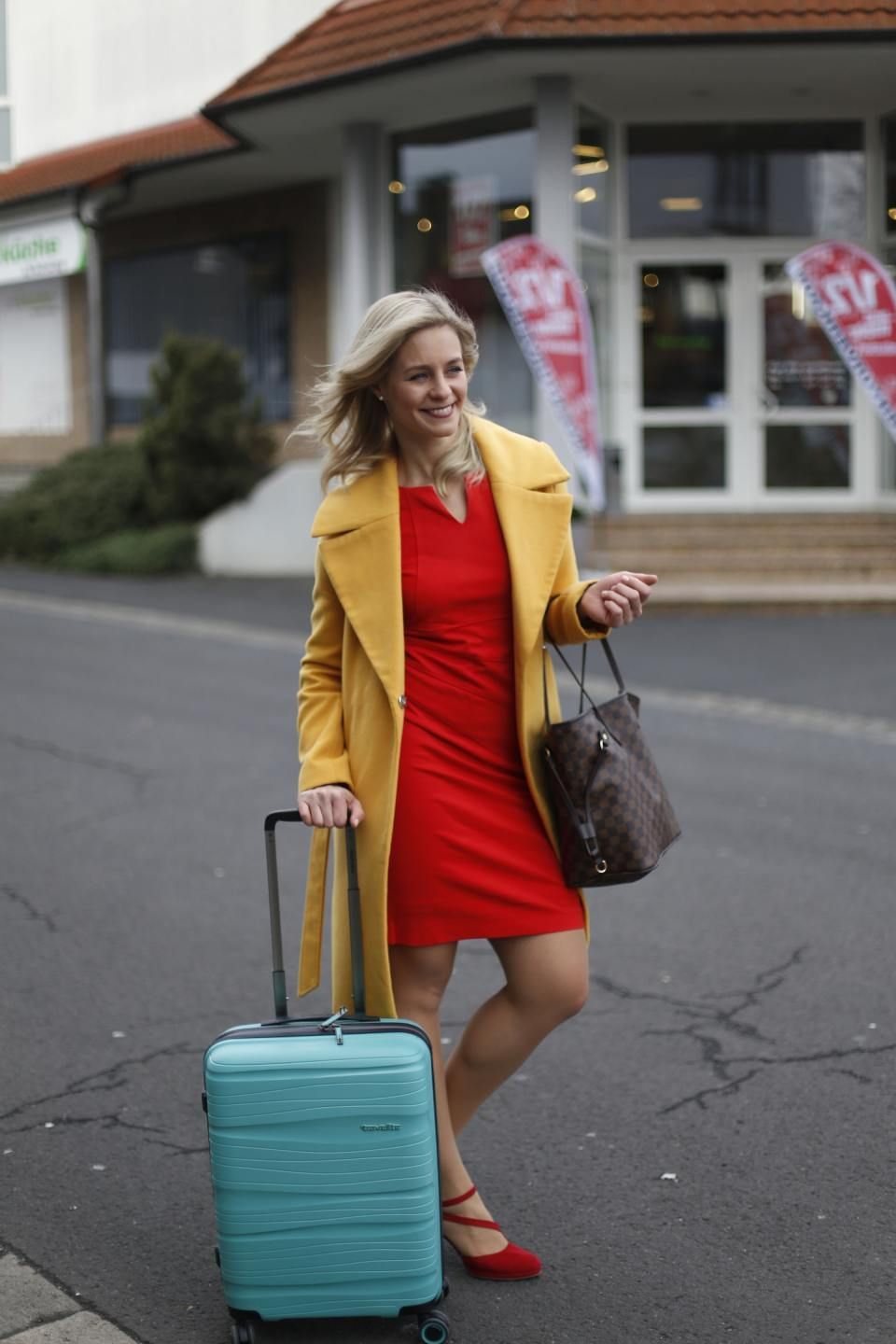 Frau im roten Kleid mit türkisem Koffer