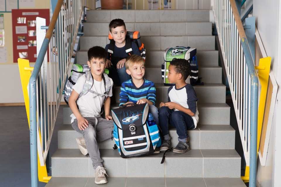 Vier Kinder sitzen auf Schultreppen mit ihren Rucksäcken