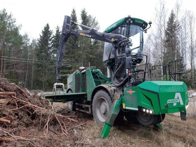 Vihreä metsäkone metsässä, toiminnassa ojennettuna olevalla varrella, tukkikasan lähellä.