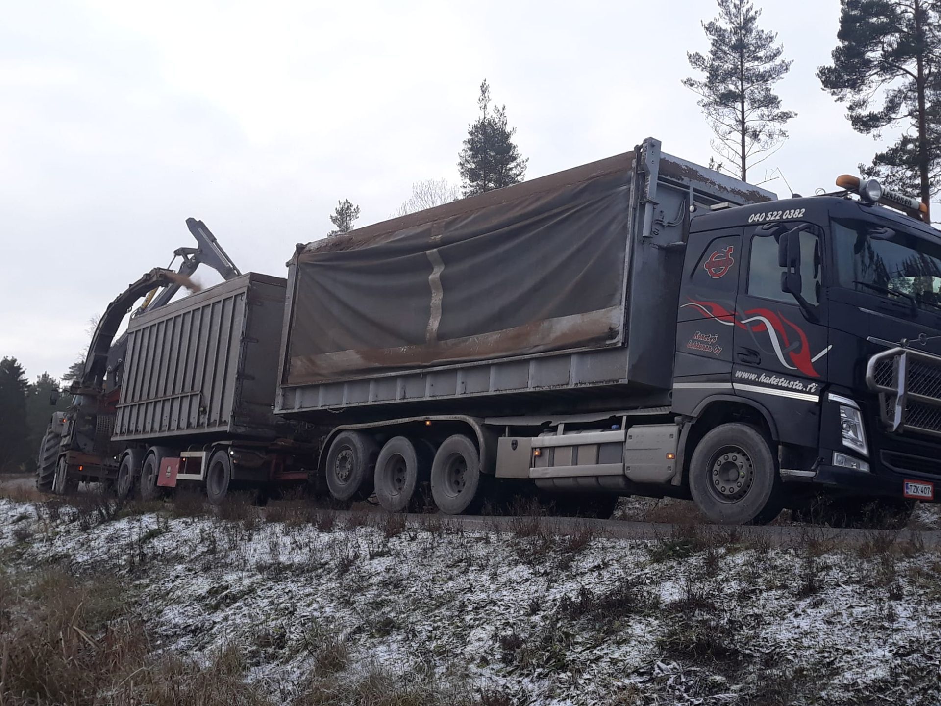 Kuorma-auto lastaa maata lumisessa metsässä.