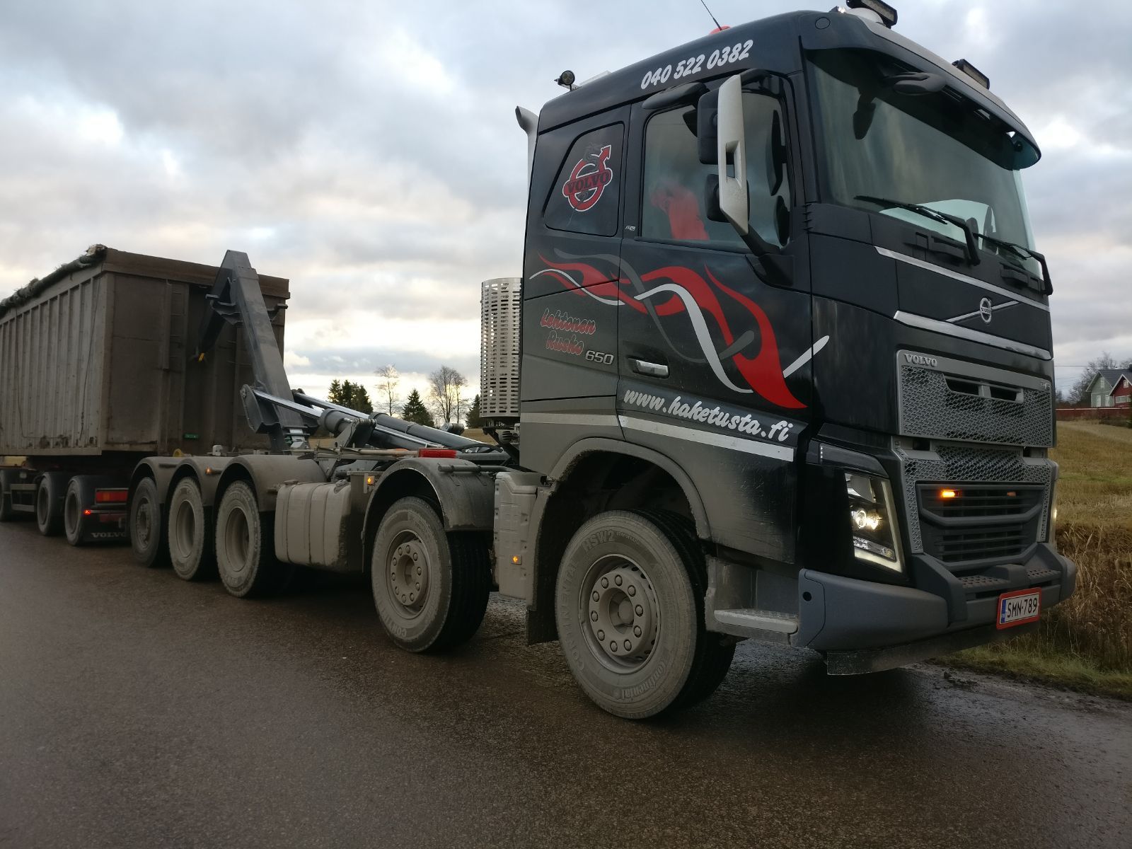 Musta rekka vetää materiaalilla täytettyä perävaunua tiellä pilvisellä taivaalla.