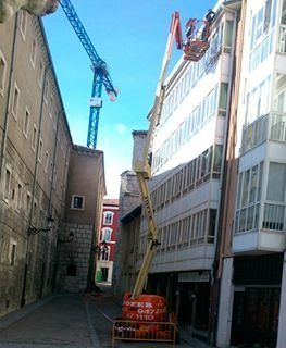 Un ascensor de construcción llega a la parte superior de un edificio de apartamentos de varios pisos en una estrecha calle urbana.