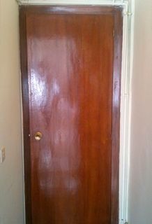 Una puerta de madera pulida de color marrón medio con una sencilla perilla redonda dorada colocada en un marco de pared blanco.