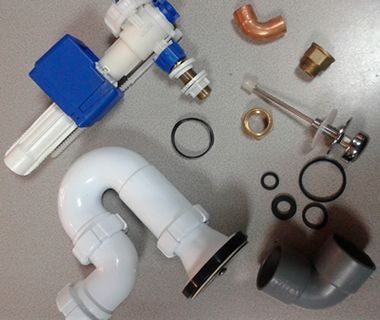 Una colección de componentes de plomería, que incluye una válvula de llenado de inodoro, una trampa P blanca, juntas y conectores de tuberías variados.