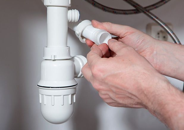 Manos ensamblando componentes de plomería de plástico blanco debajo de un fregadero.