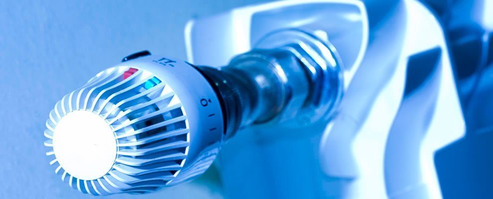 Primer plano de una válvula termostática blanca de un radiador calefactor, capturada con una luz teñida de azul.