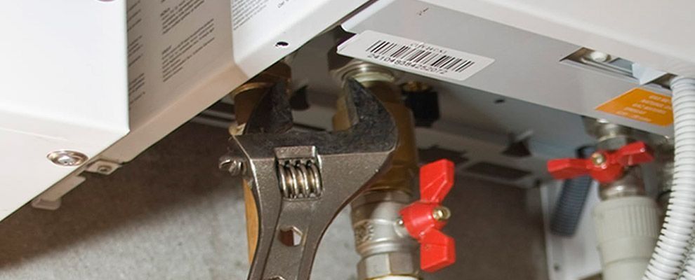 Llave ajustable que aprieta una tuerca de latón en la parte inferior de una unidad de calentador de agua blanco con manijas de válvula rojas.