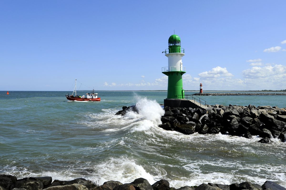 Ein grün-weißer Leuchtturm steht inmitten eines Gewässers.