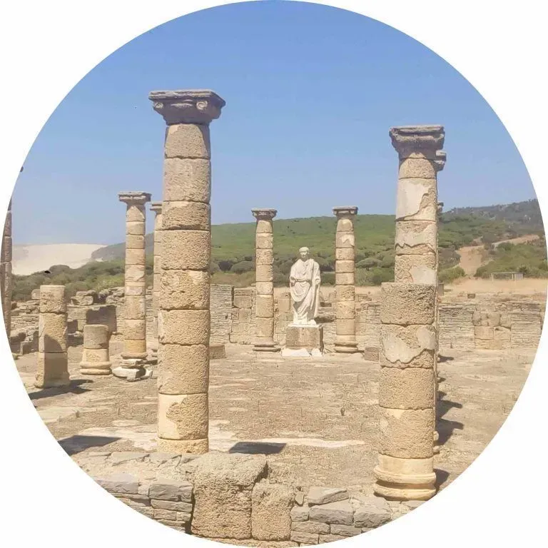 Antiguas ruinas de piedra con columnas y una estatua bajo un cielo azul despejado.