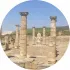 Antiguas ruinas de piedra con columnas y una estatua bajo un cielo azul despejado.