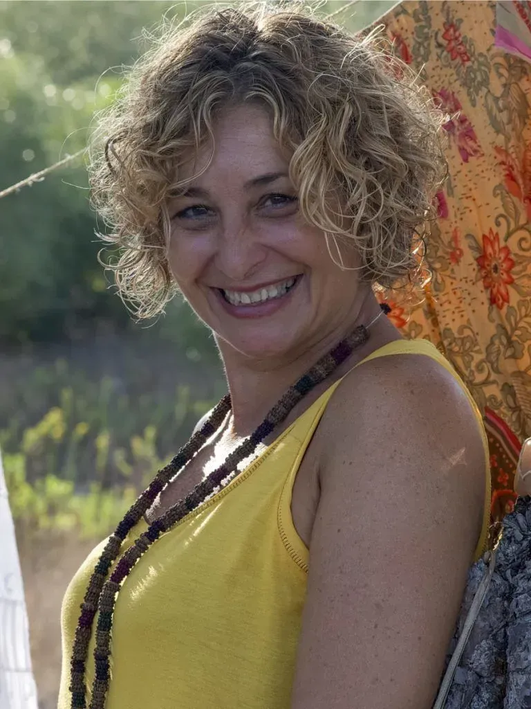 Persona sonriente con una blusa amarilla apoyada en un árbol al aire libre