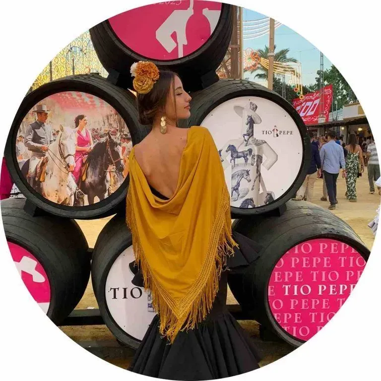 Mujer con un vestido drapeado color mostaza posando frente a paneles circulares de exhibición de moda al aire libre.