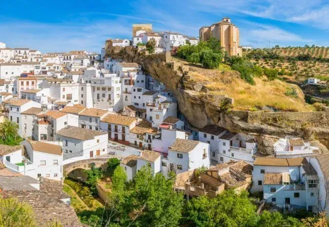 Pueblo blanco en la ladera de una colina con casas encaladas y una fortaleza de piedra en una cresta rocosa.
