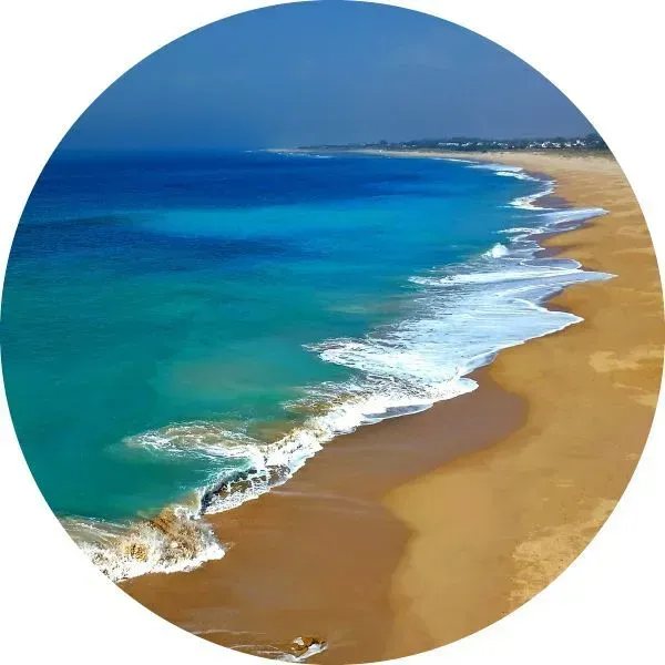 Vista aérea de olas turquesas rompiendo en una playa de arena bajo un cielo azul claro.