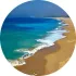Vista aérea de olas turquesas rompiendo en una playa de arena bajo un cielo azul claro.