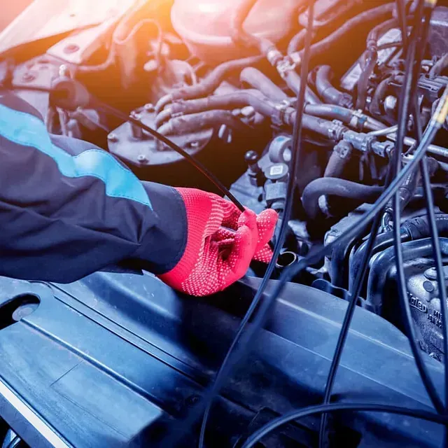 Mecánico con guante rojo trabajando en un motor de automóvil con herramientas de diagnóstico.
