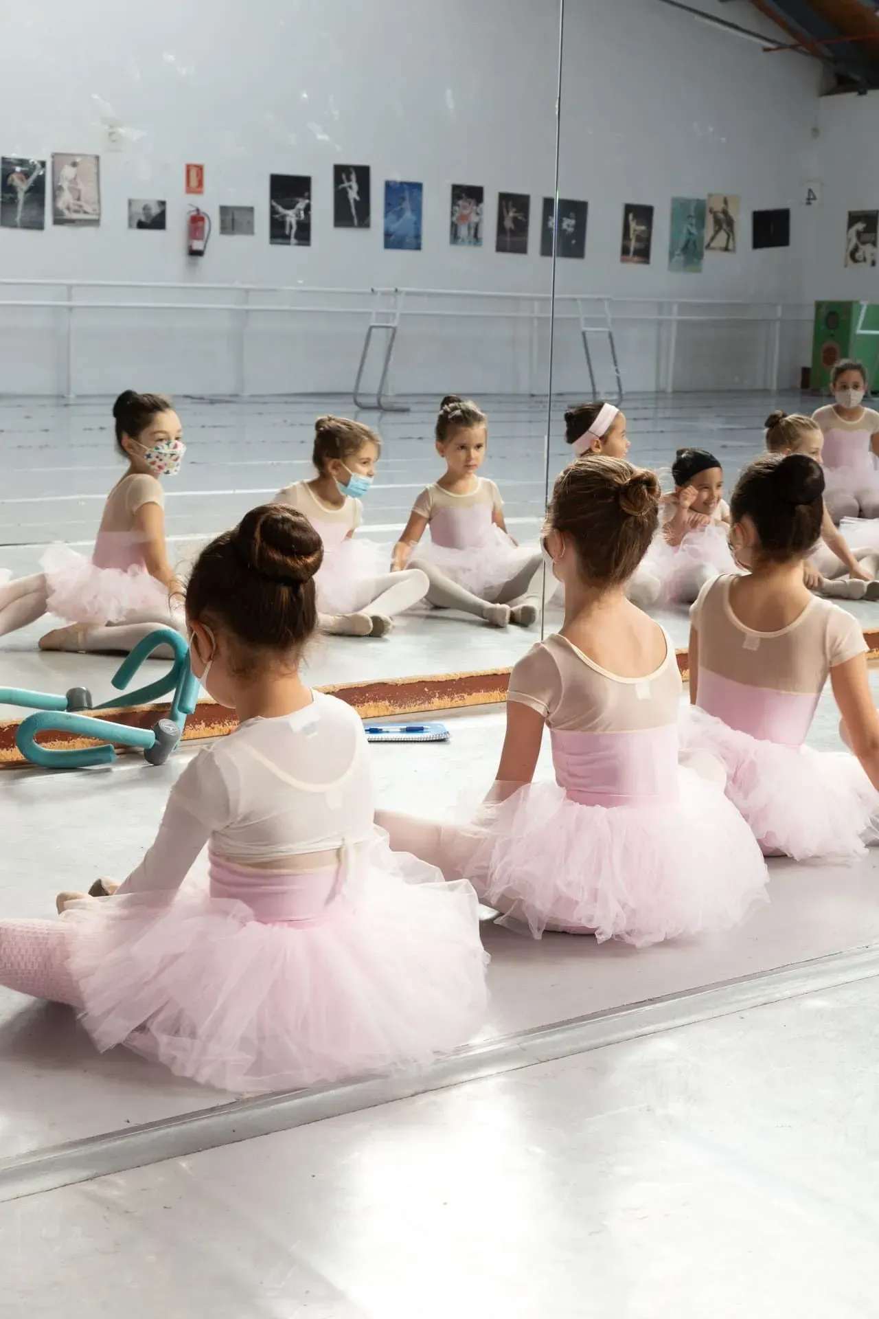Niñas con tutús rosas sentadas en un estudio de clases de ballet, vistas desde atrás.