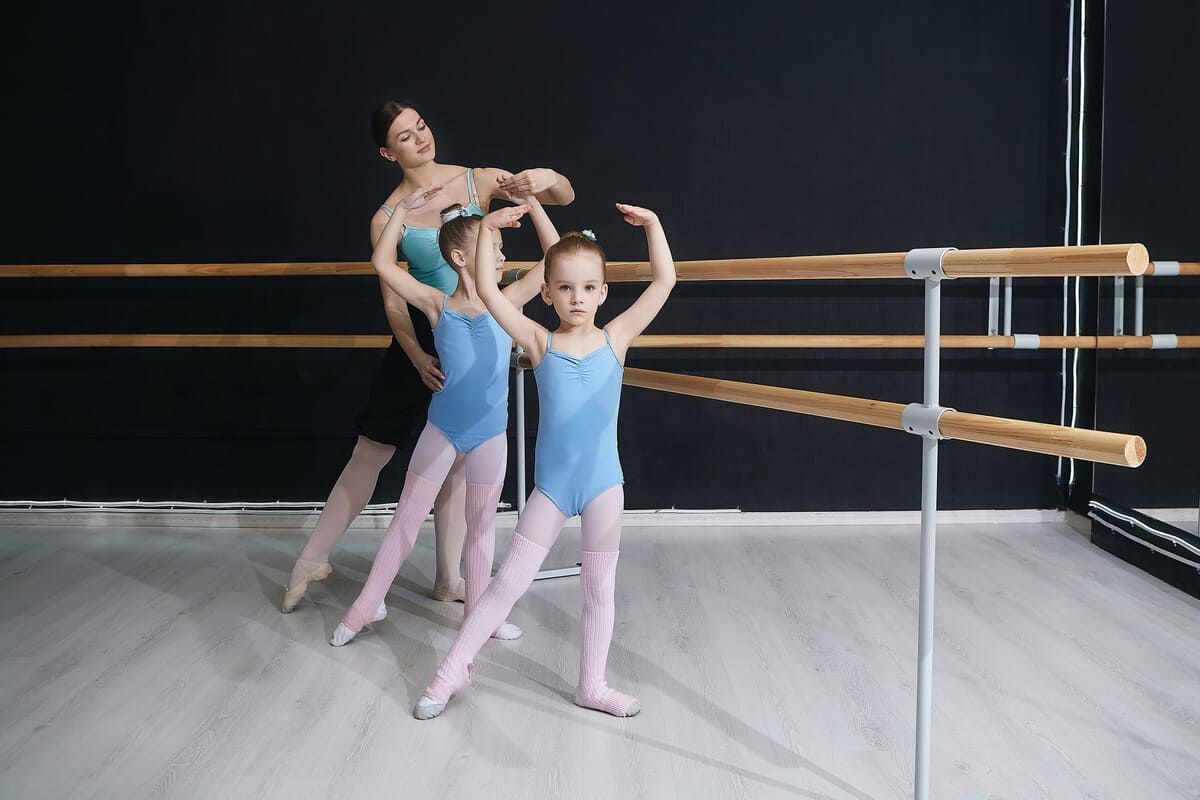 Tres bailarinas de ballet con leotardos azules practican en una barra en un estudio.