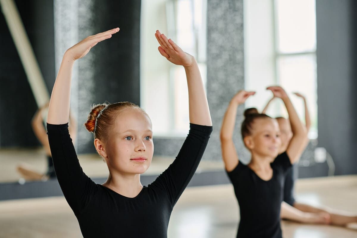 Dos bailarinas con leotardos negros practicando posiciones de brazos de ballet en un estudio.