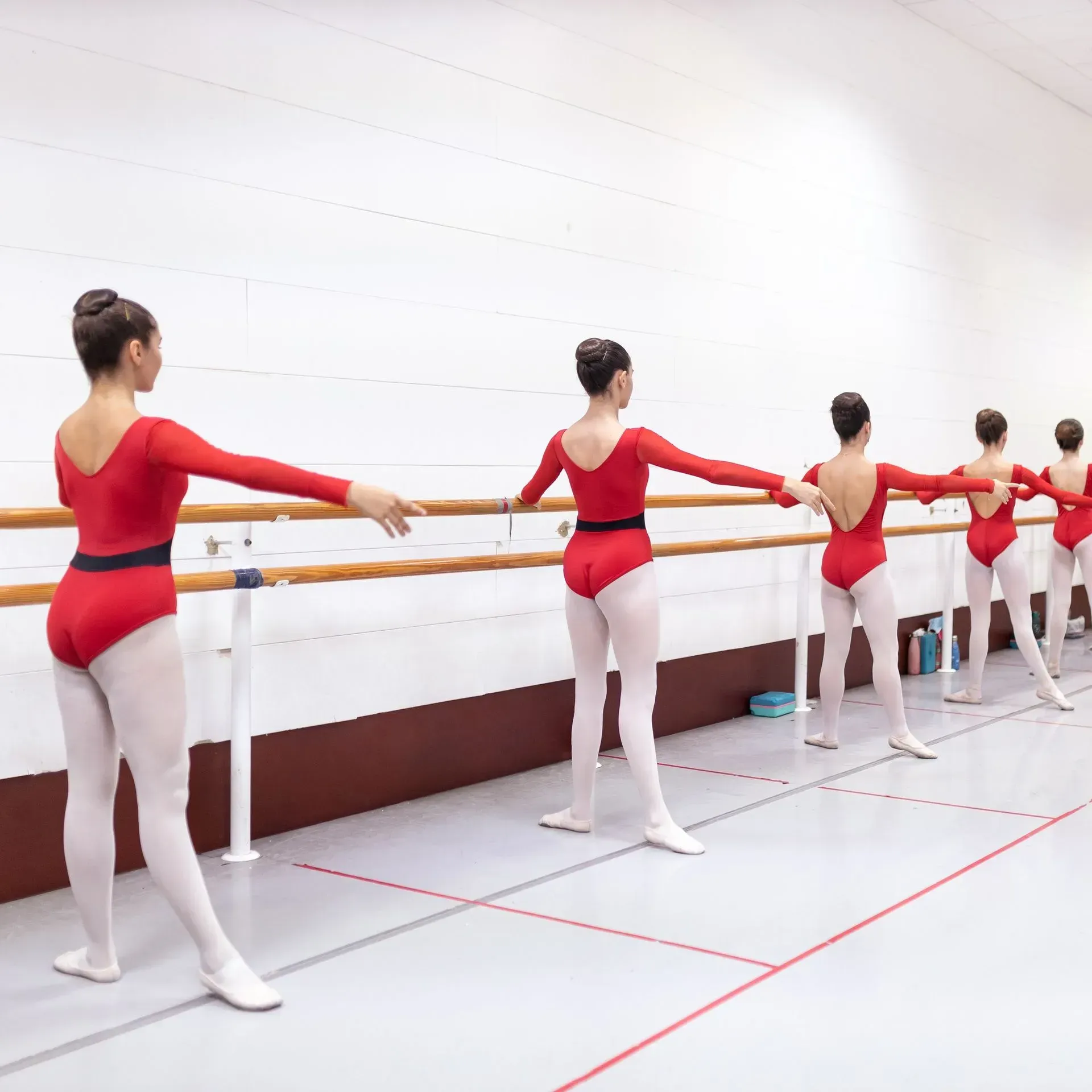 Bailarinas de ballet con leotardos rojos practicando en una barra en un estudio luminoso.