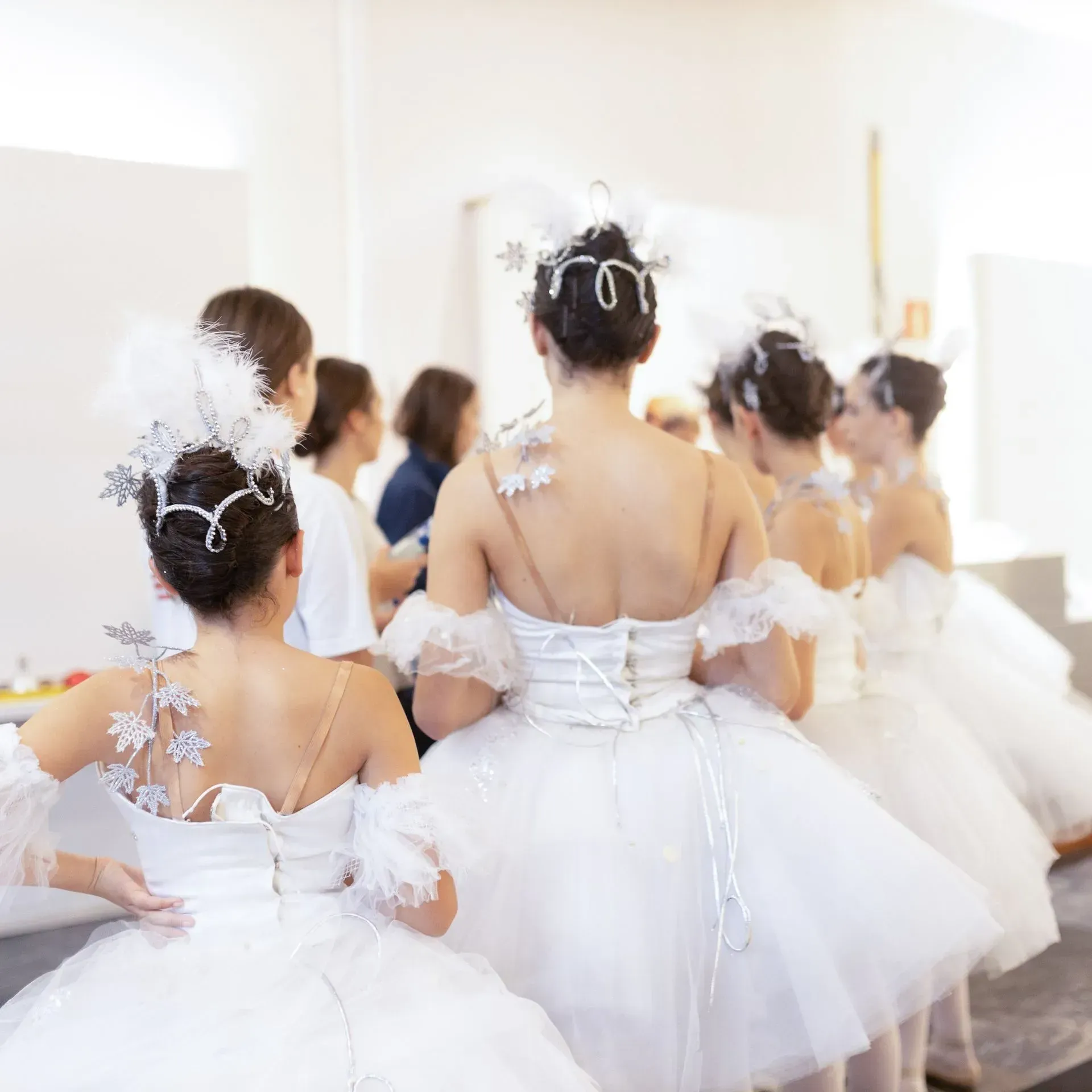 Bailarinas de ballet con tutús blancos de pie en un estudio luminoso, vistas desde atrás.
