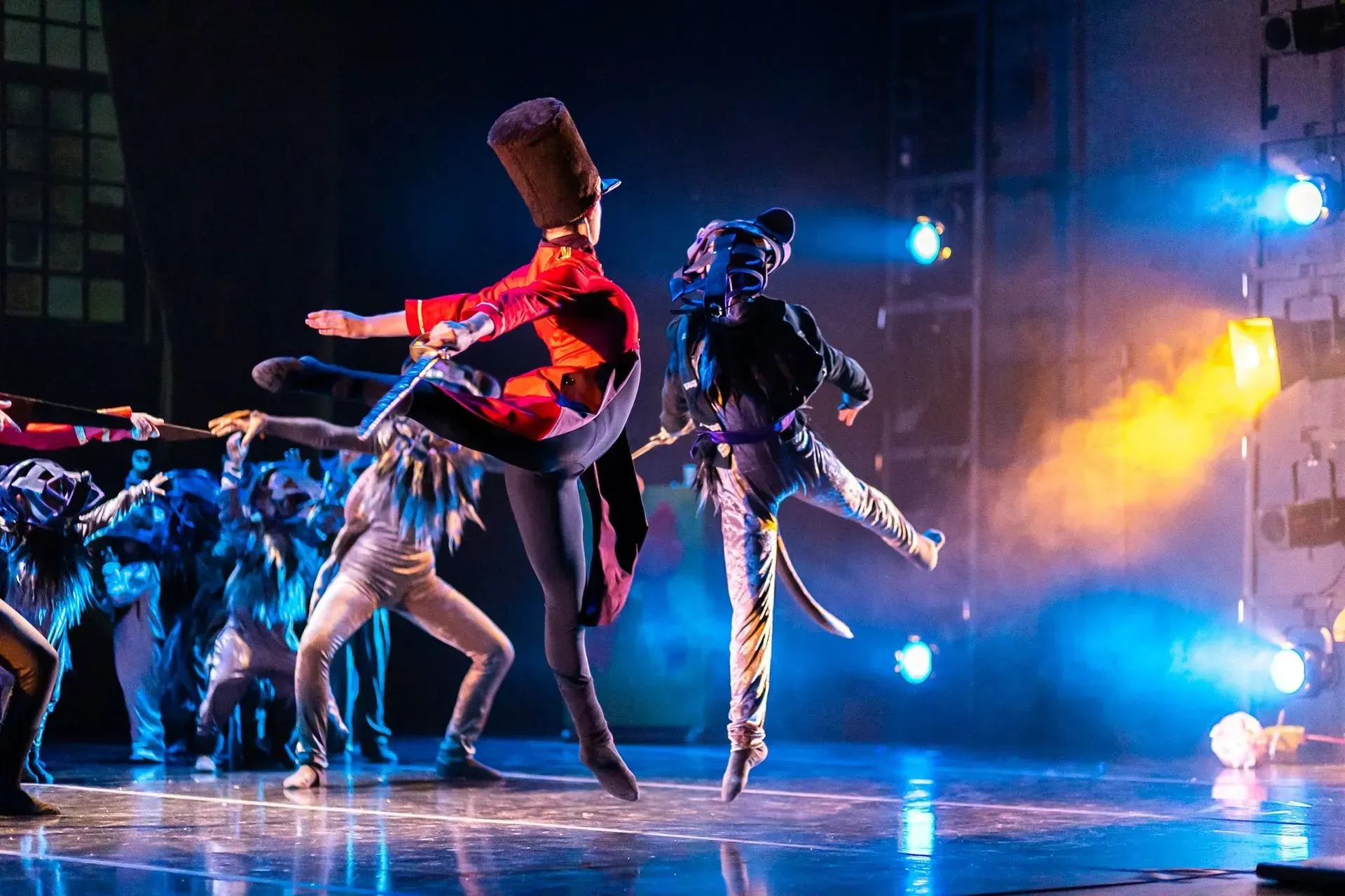 Bailarines con coloridos trajes interpretan una rutina dramática en un escenario iluminado con luces azules y naranjas.
