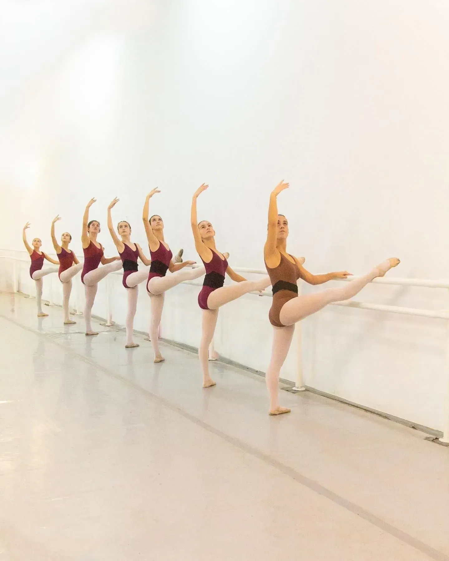 Bailarines de ballet en un estudio, practicando una serie de extensiones de piernas altas en la barra.