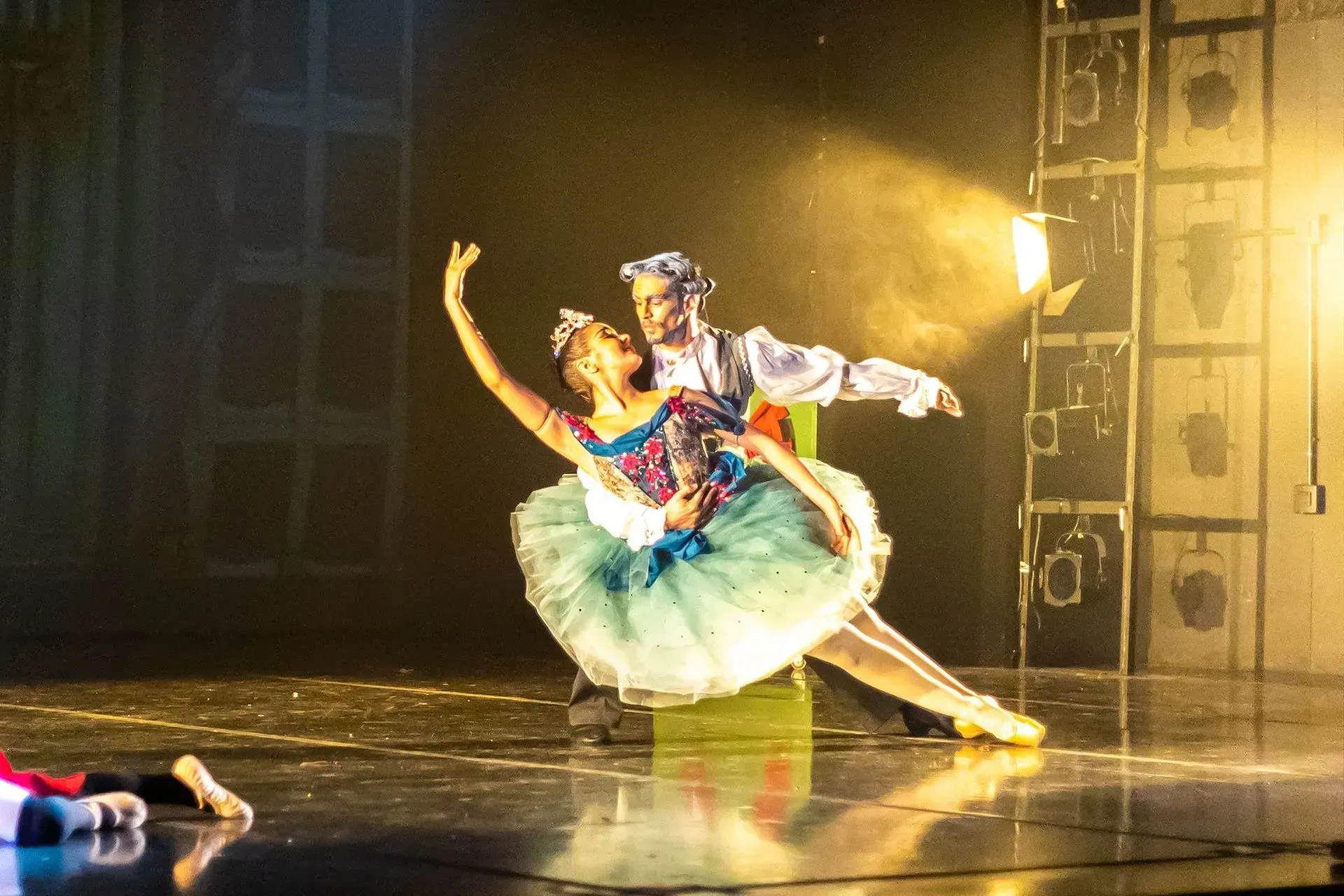 Dos bailarinas de ballet con trajes en tonos pastel posan bajo las cálidas luces del escenario de un teatro.
