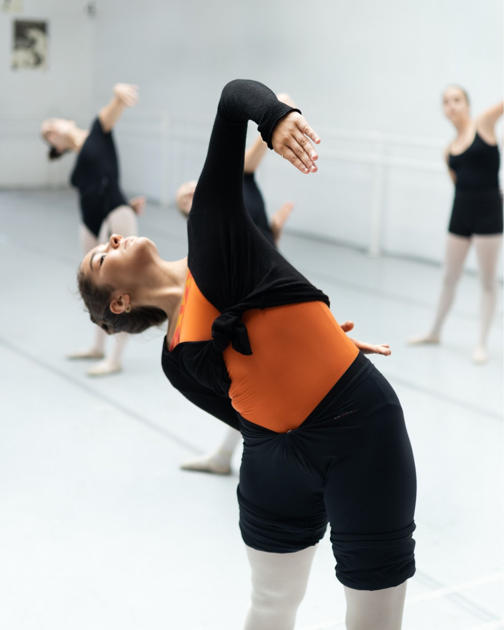 Una mujer con una camiseta naranja está inclinada en un estudio de baile.