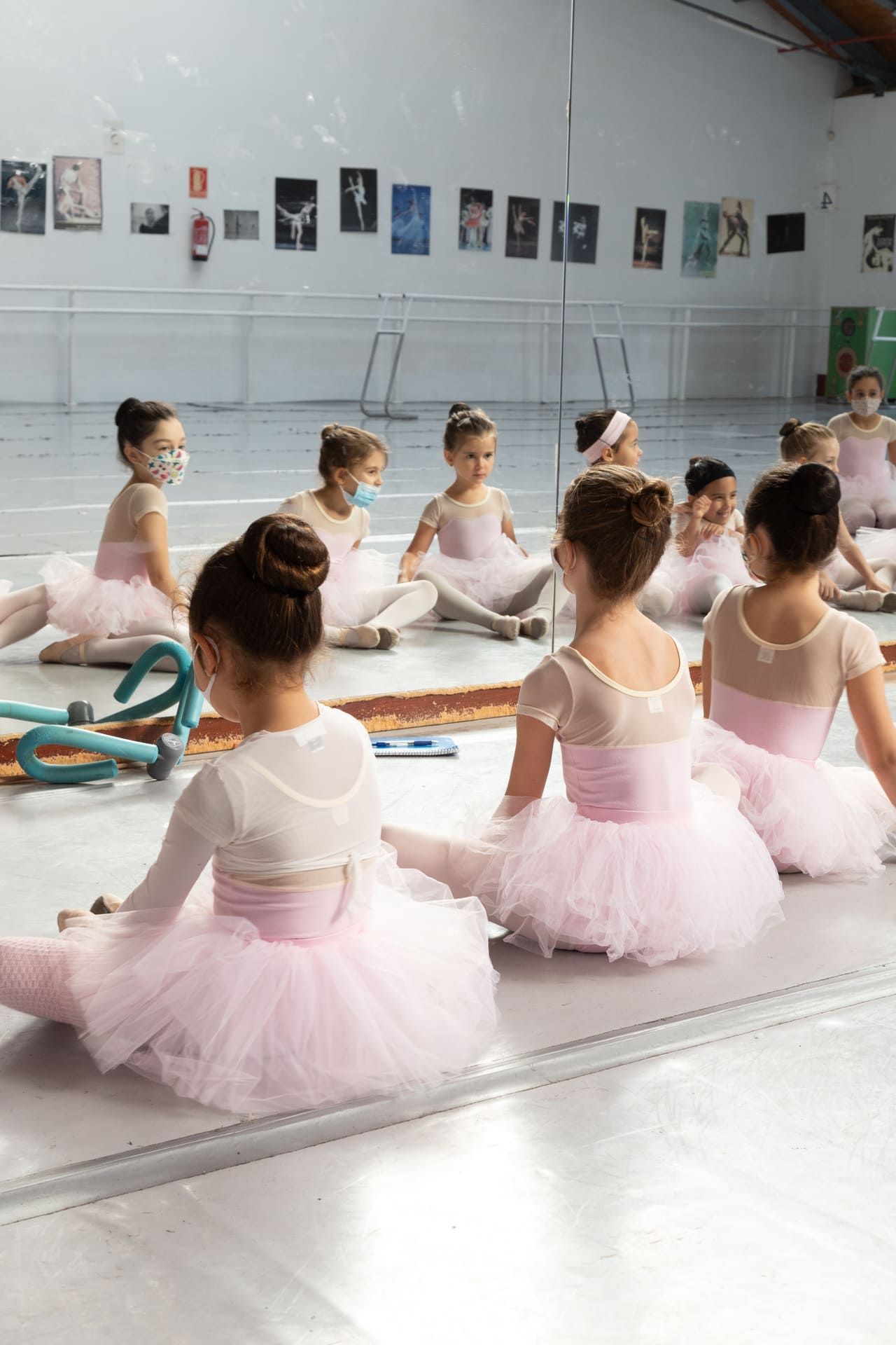 Clase de ballet con bailarinas con tutús rosas sentadas en el suelo del estudio, vista desde atrás.