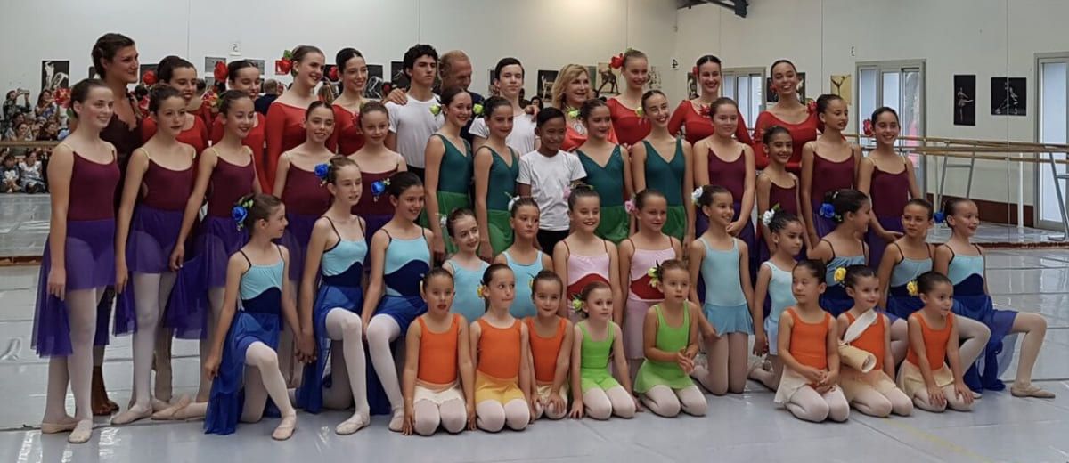 Un numeroso grupo de baile posa en un estudio, luciendo coloridos trajes y zapatillas de ballet.