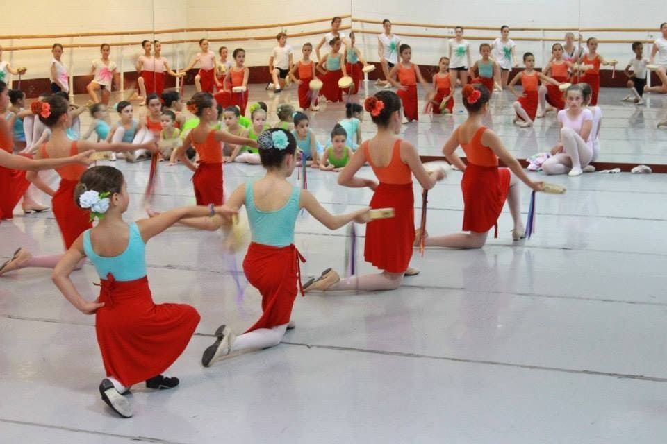 Niños con faldas rojas y blusas turquesas practicando danza sincronizada en un estudio.