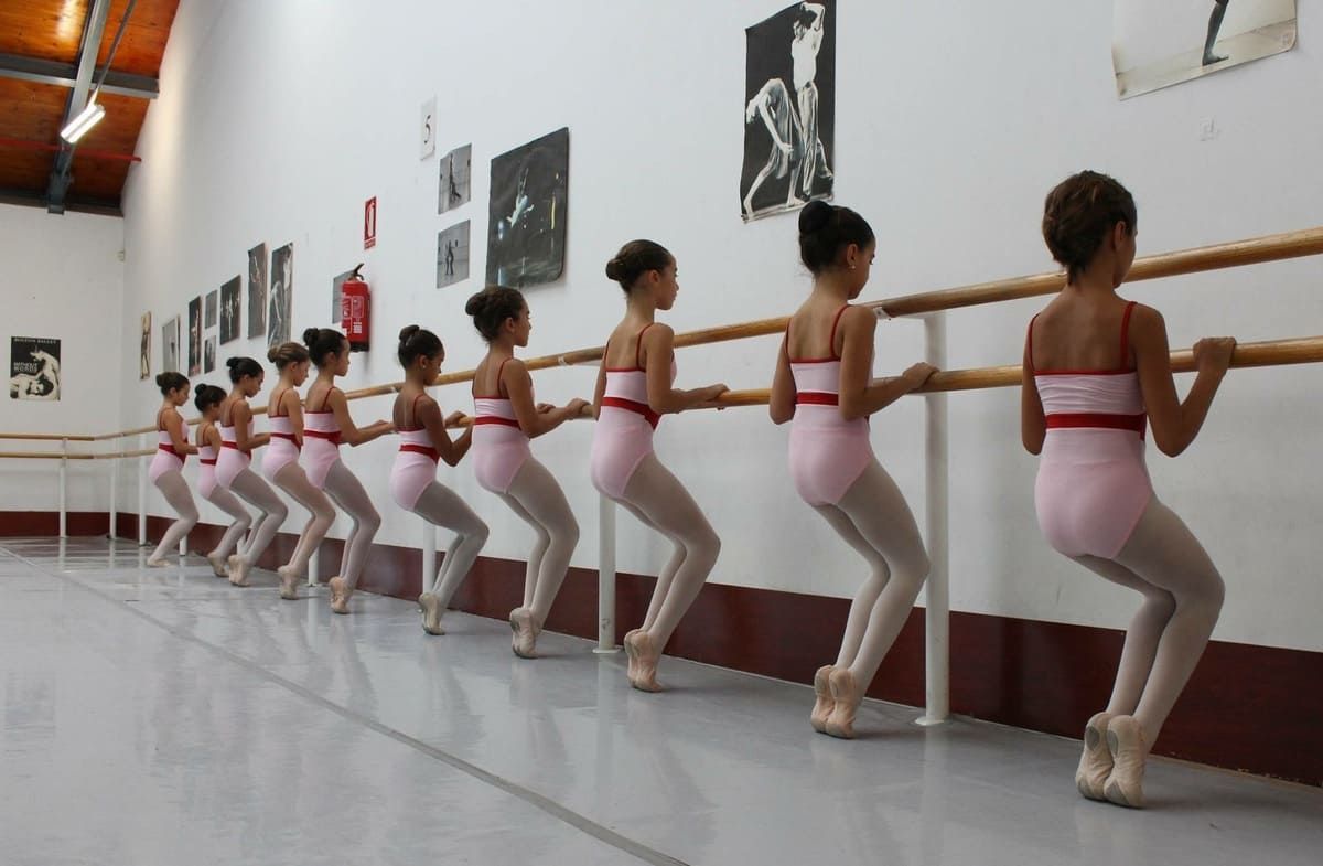 Jóvenes bailarinas de ballet con leotardos rosas practican en una barra en un estudio.