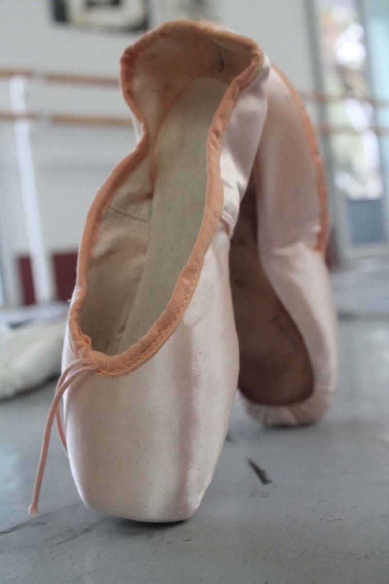 Zapatillas de punta de ballet rosas sobre el suelo, con la abertura de una de ellas orientada hacia la cámara.