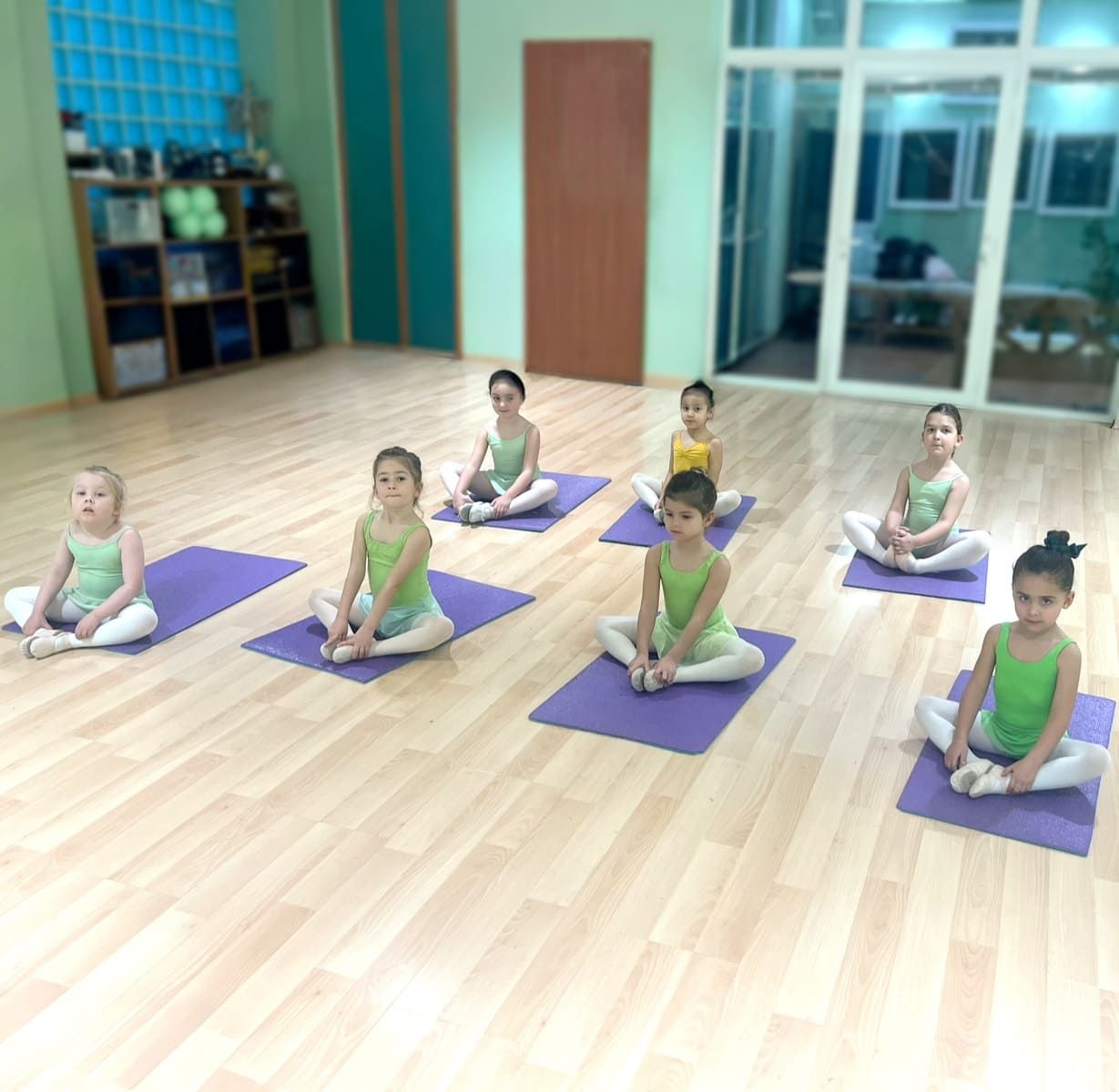 Seis niños sentados con las piernas cruzadas sobre esterillas de yoga en un estudio luminoso, practicando meditación.