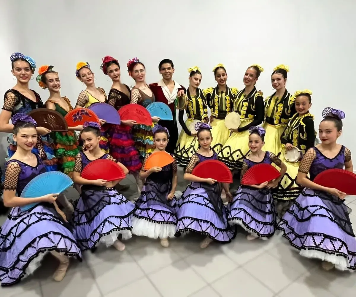 Un grupo de bailarines con coloridos trajes folclóricos posan con sus fans en el escenario.