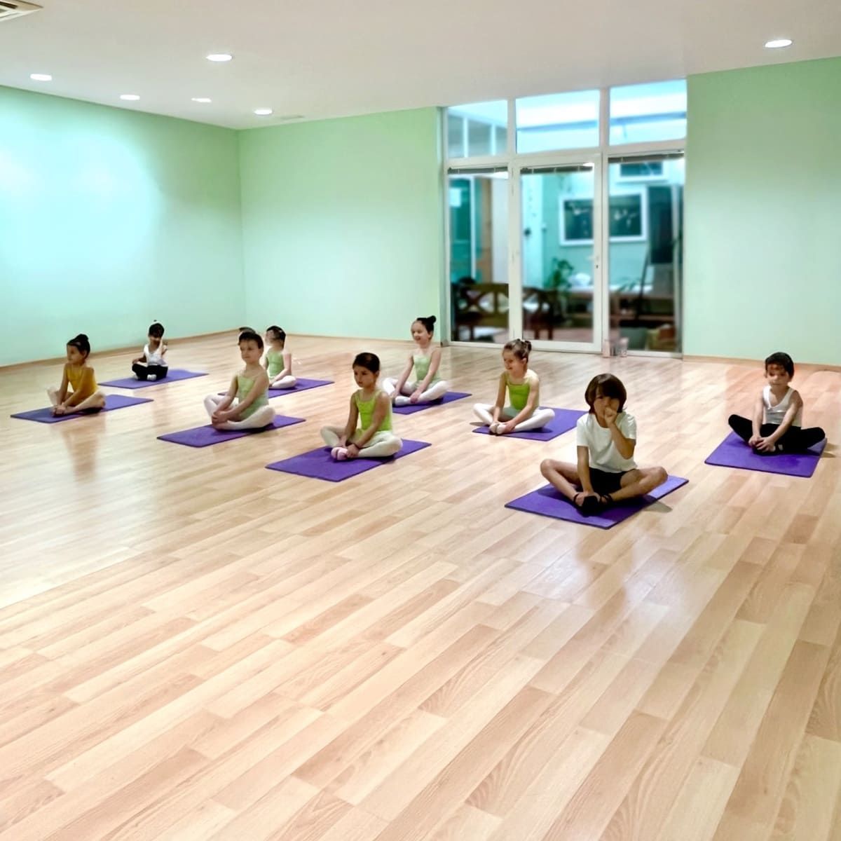 Niños practicando yoga sobre esterillas moradas en un estudio luminoso con suelo de madera.