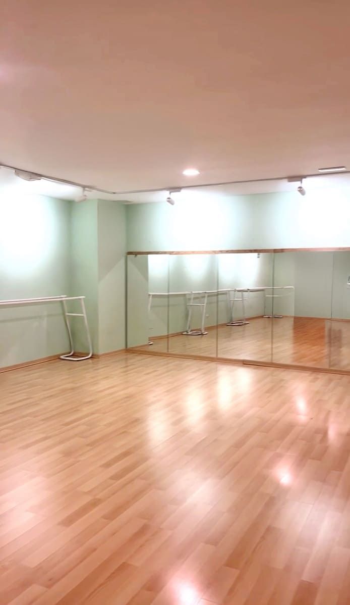 Estudio de danza vacío con suelo de madera, pared con espejo, paredes de color verde menta y barras de ballet.