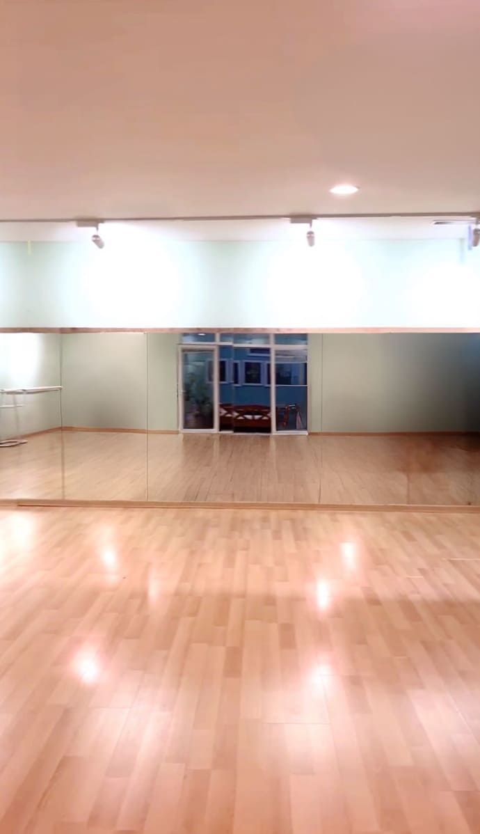 Estudio de danza vacío con suelo de madera pulida, pared con espejos y luces brillantes en el techo.