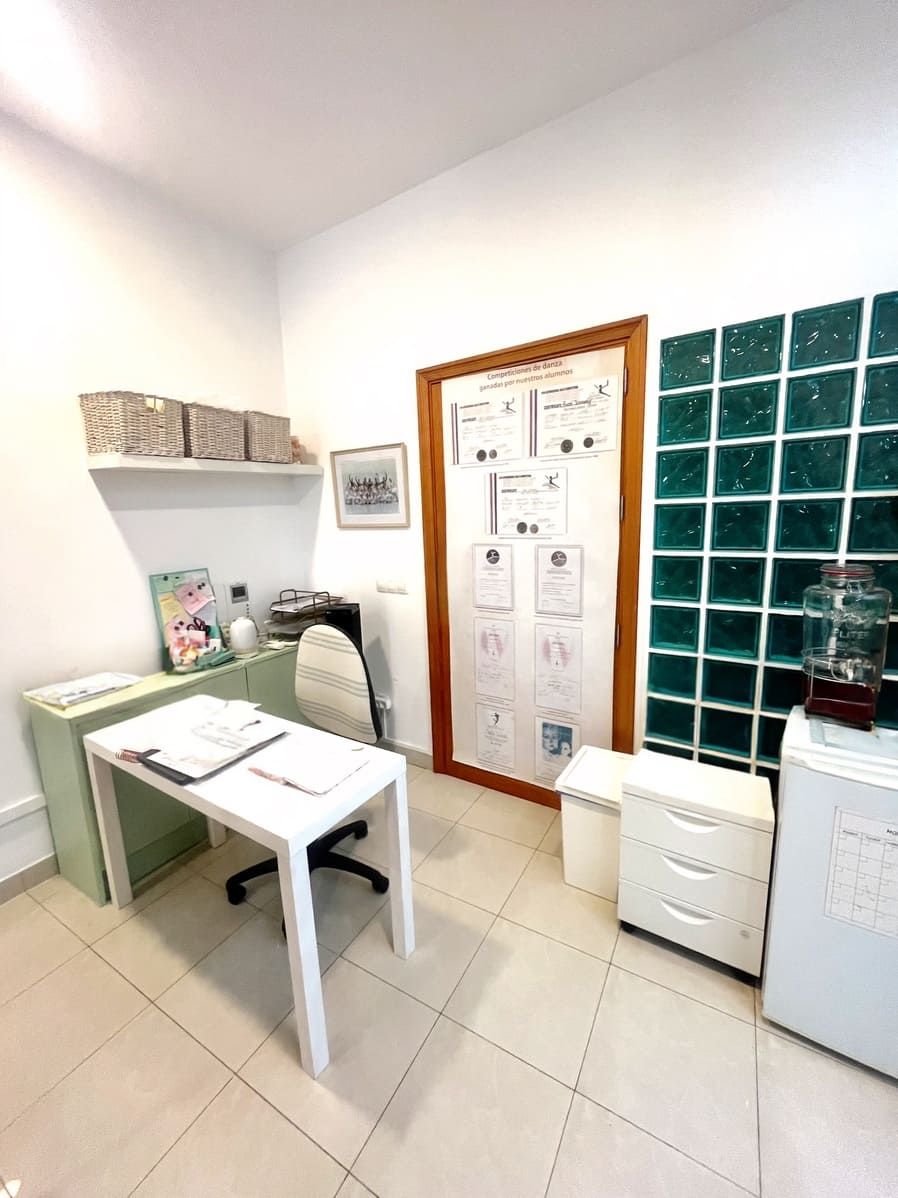 Pequeña oficina con escritorio, silla blanca, organizadores de pared y mampara de bloques de vidrio verde en una habitación alicatada.