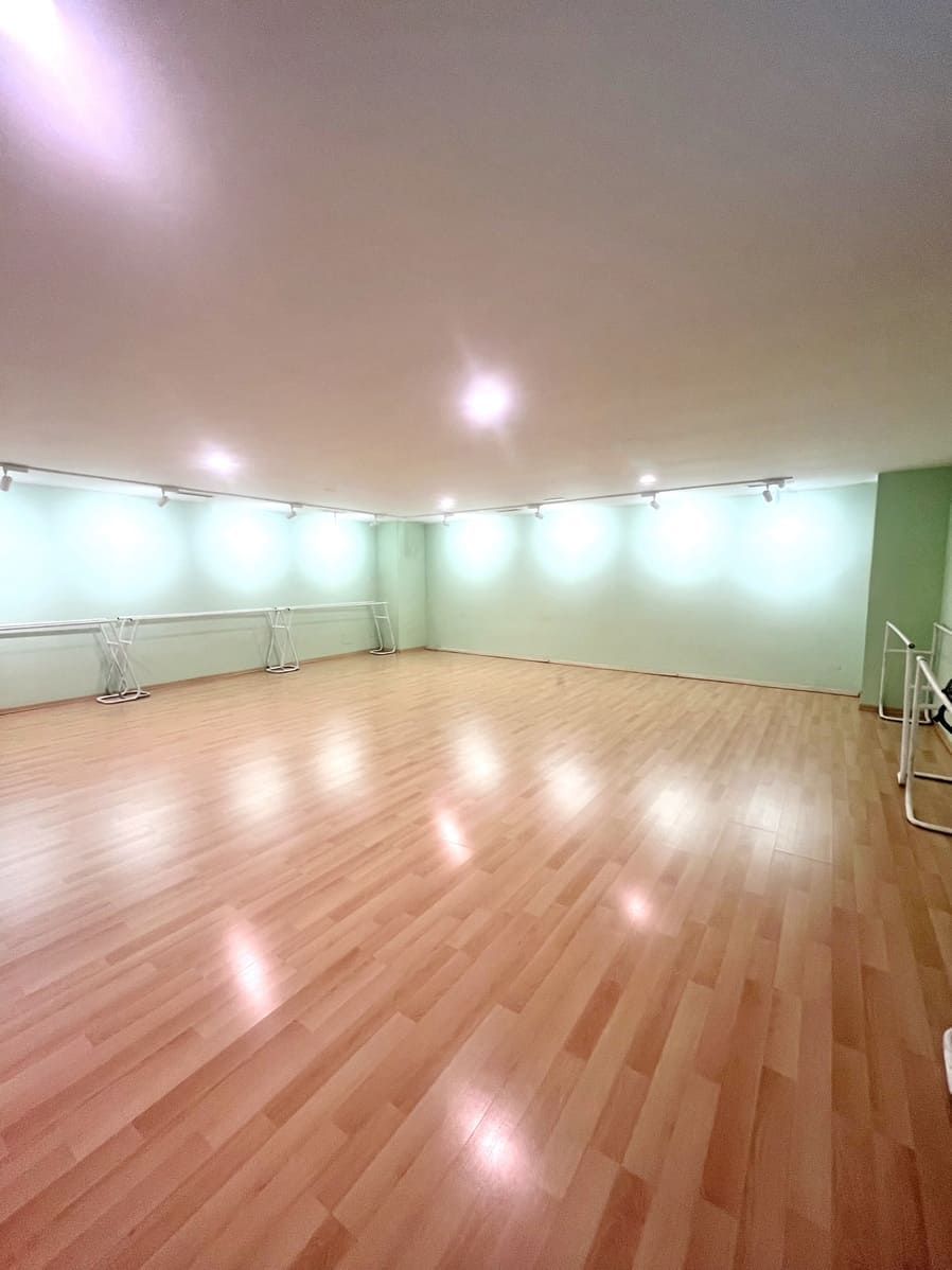 Estudio de danza vacío con suelo de madera pulida, paredes de color verde pálido y luces en el techo.
