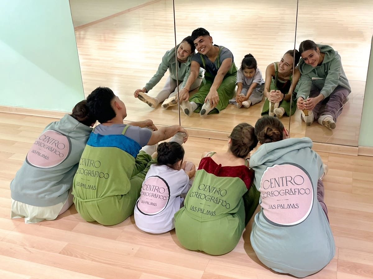 Grupo de niños sentados en círculo sobre un suelo de madera, participando en una actividad en el aula con un profesor.