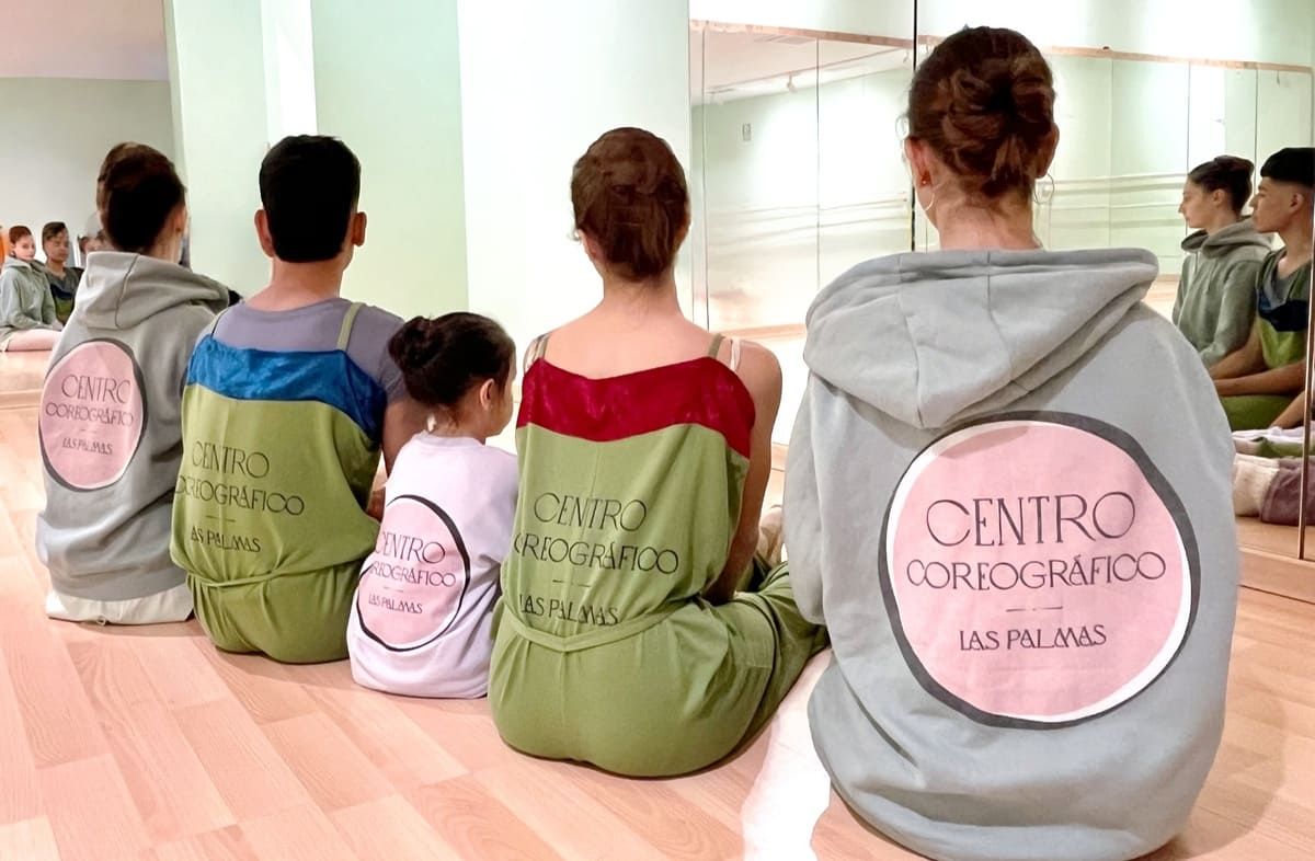 Personas sentadas sobre esterillas de yoga en un estudio, vistas desde atrás, con sudaderas verdes y grises a juego.