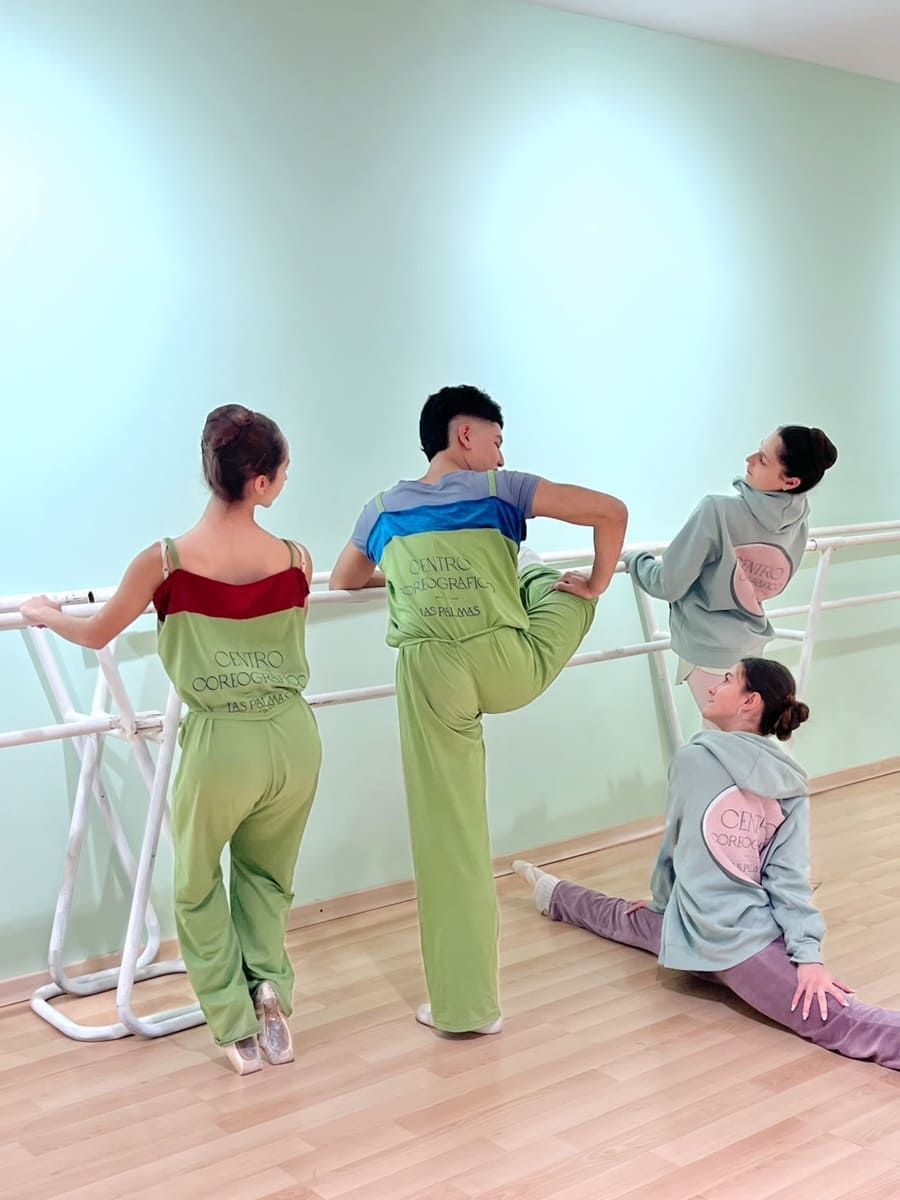 Cuatro personas se estiran en un estudio de danza, apoyadas en las barras de ballet cerca de un espejo en la pared.