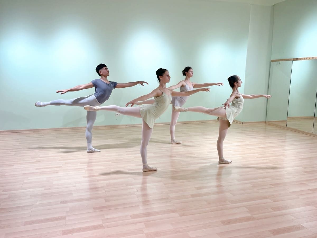 Tres bailarinas de ballet posando en arabesco en un estudio luminoso, reflejadas en un espejo de pared.