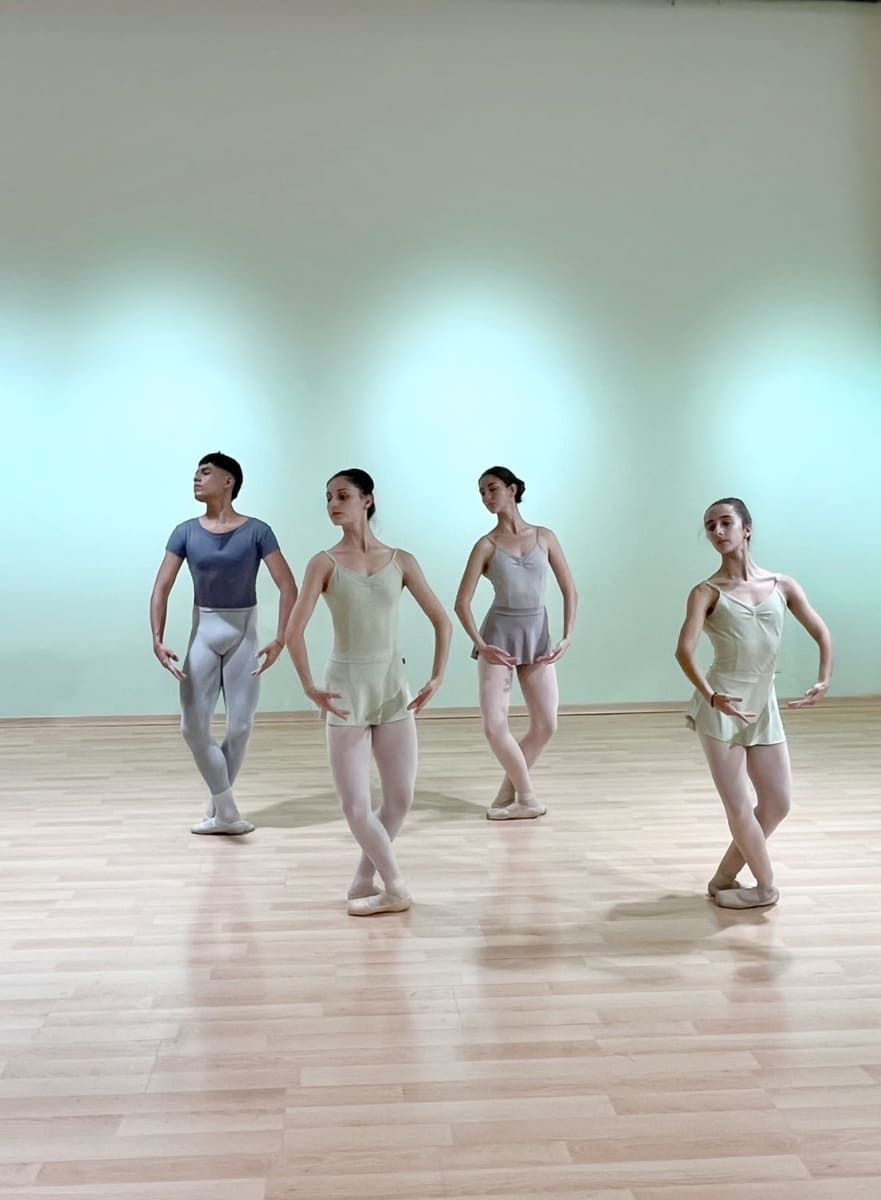 Cuatro bailarinas con trajes de ensayo en tonos pastel posan en un estudio luminoso con suelo de madera.