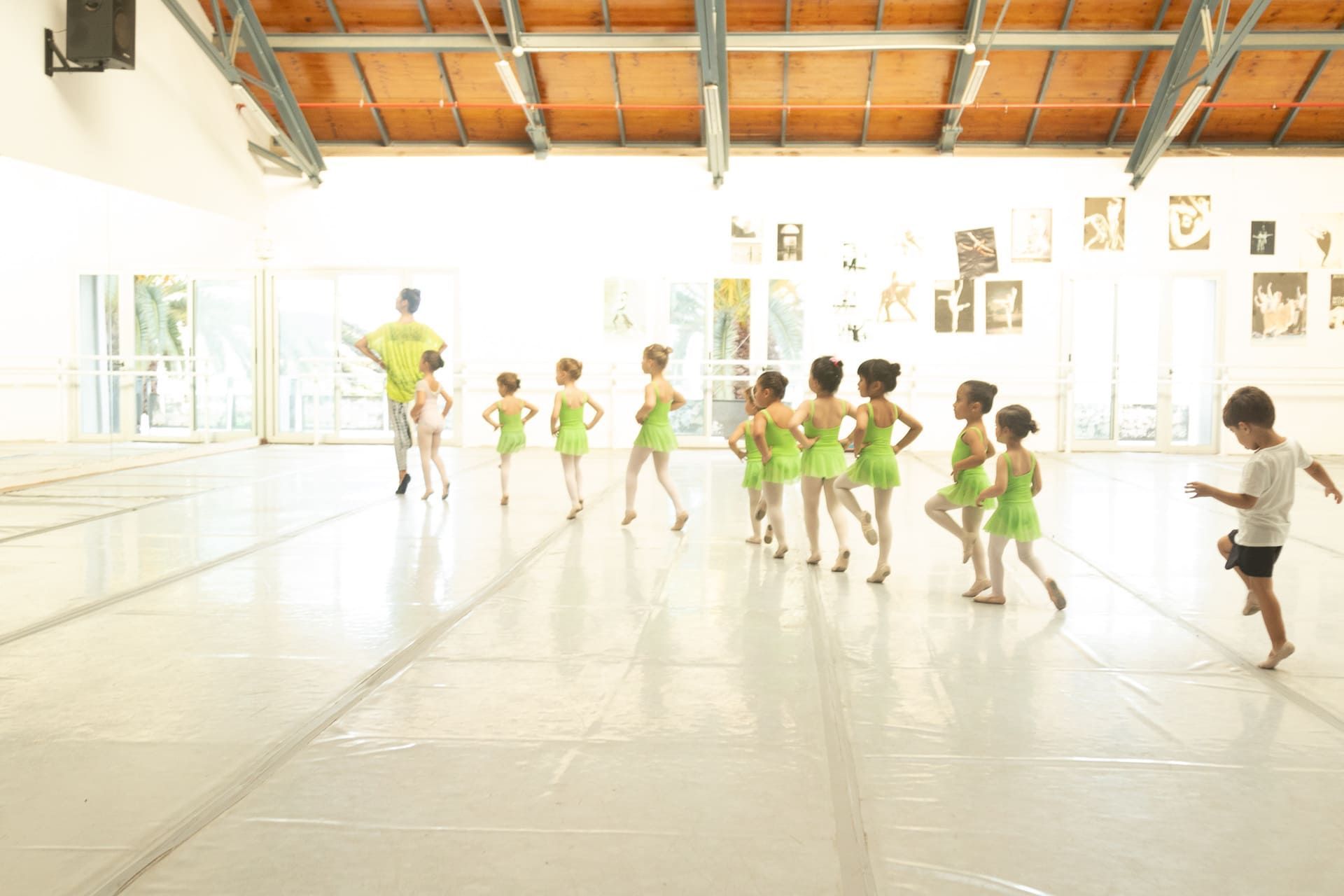 Niños vestidos con trajes de baile verdes practican en un estudio luminoso bajo la dirección de una profesora.
