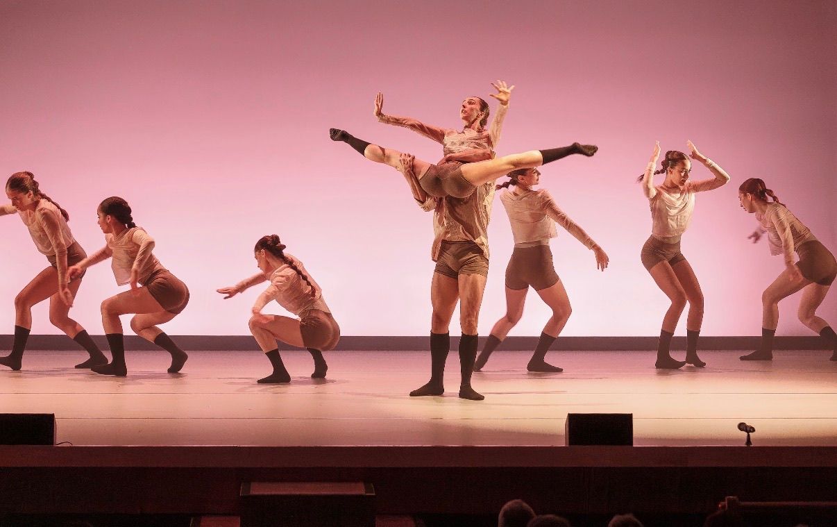 Bailarines realizando una coreografía sincronizada en un escenario con iluminación rosa.