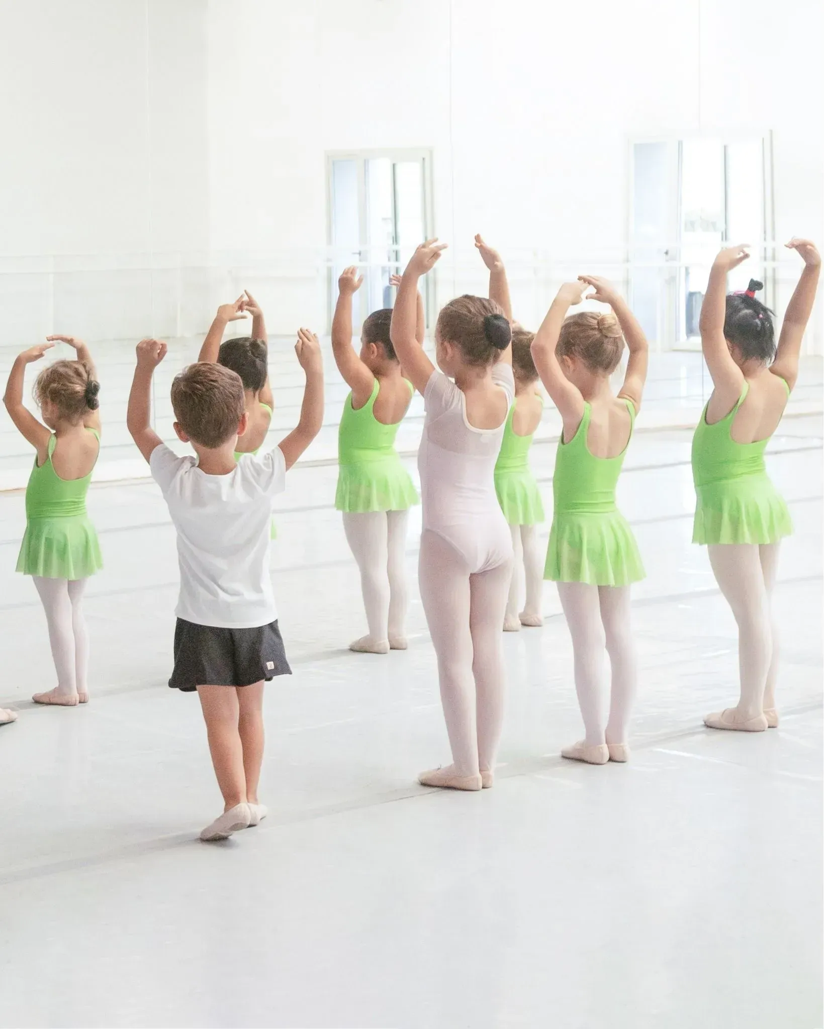 Niños con trajes de ballet practicando posturas de baile en un estudio luminoso.