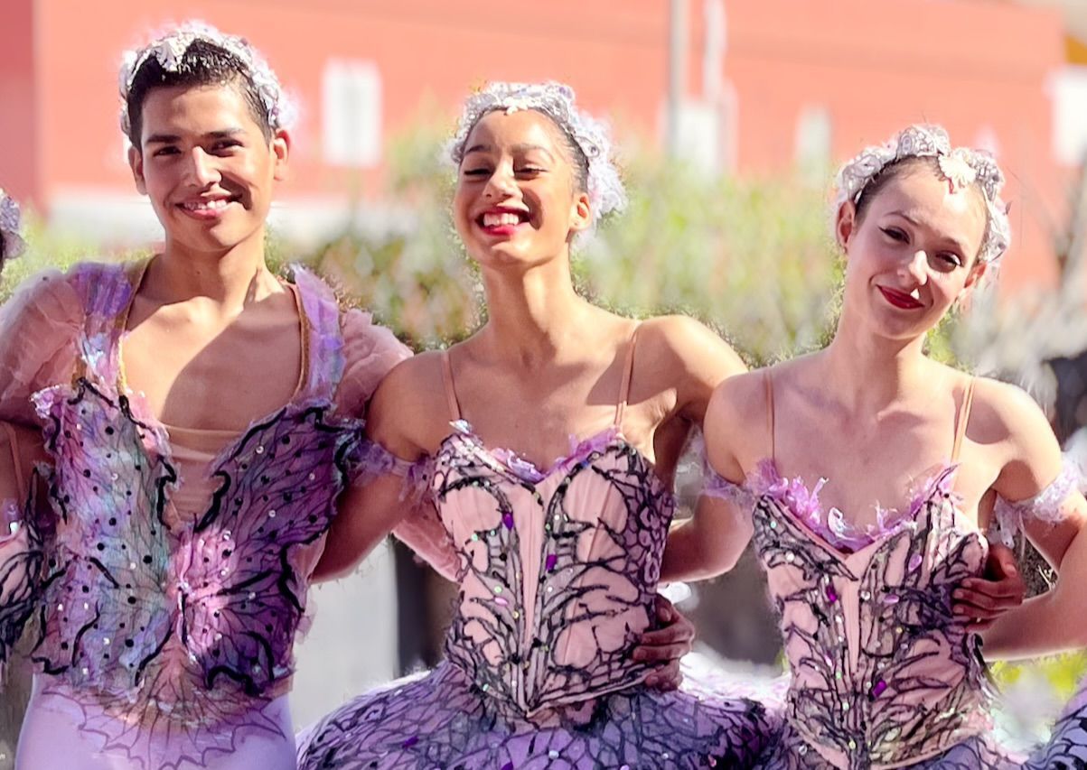 Tres bailarinas de ballet con trajes morados sonríen al aire libre durante una actuación.